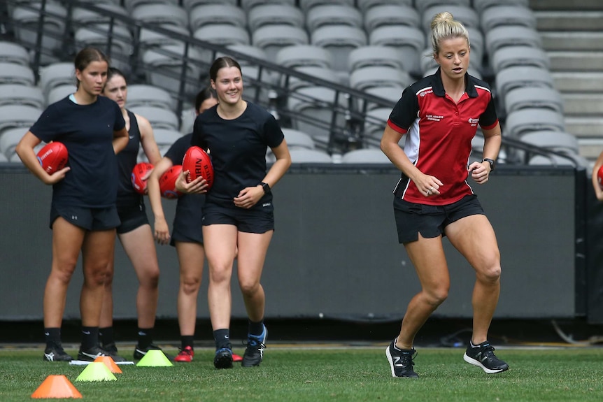 A woman leads the way in a running drill while junior players look on