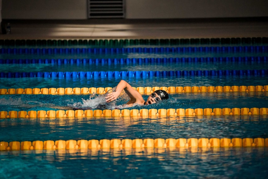 A swimmer completes side stroke between lane ropes.