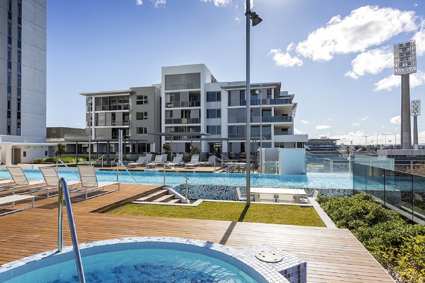 A fourth floor pool deck at the Queens Riverside development in Perth under sunshine with WACA light towers in the distance.