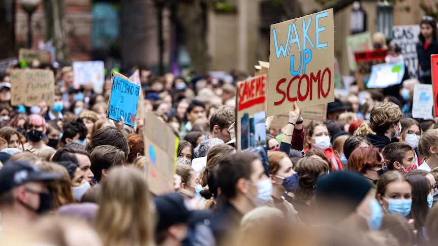 A large crowd of young people hold up signs in protest. One reads "WAKE UP SCOMO".