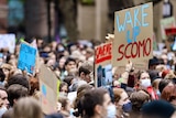 A large crowd of young people hold up signs in protest. One reads "WAKE UP SCOMO".