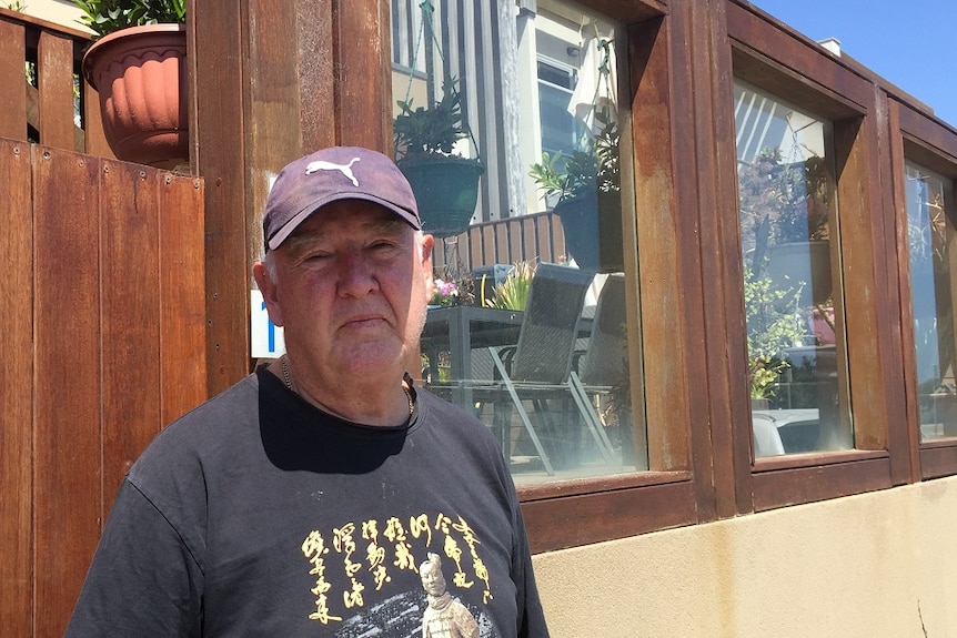 Graham Arvidson stands in front of a wall outside his property wearing a t-shirt and cap.