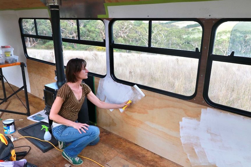 A woman uses a roller to paint the interior of a bus white