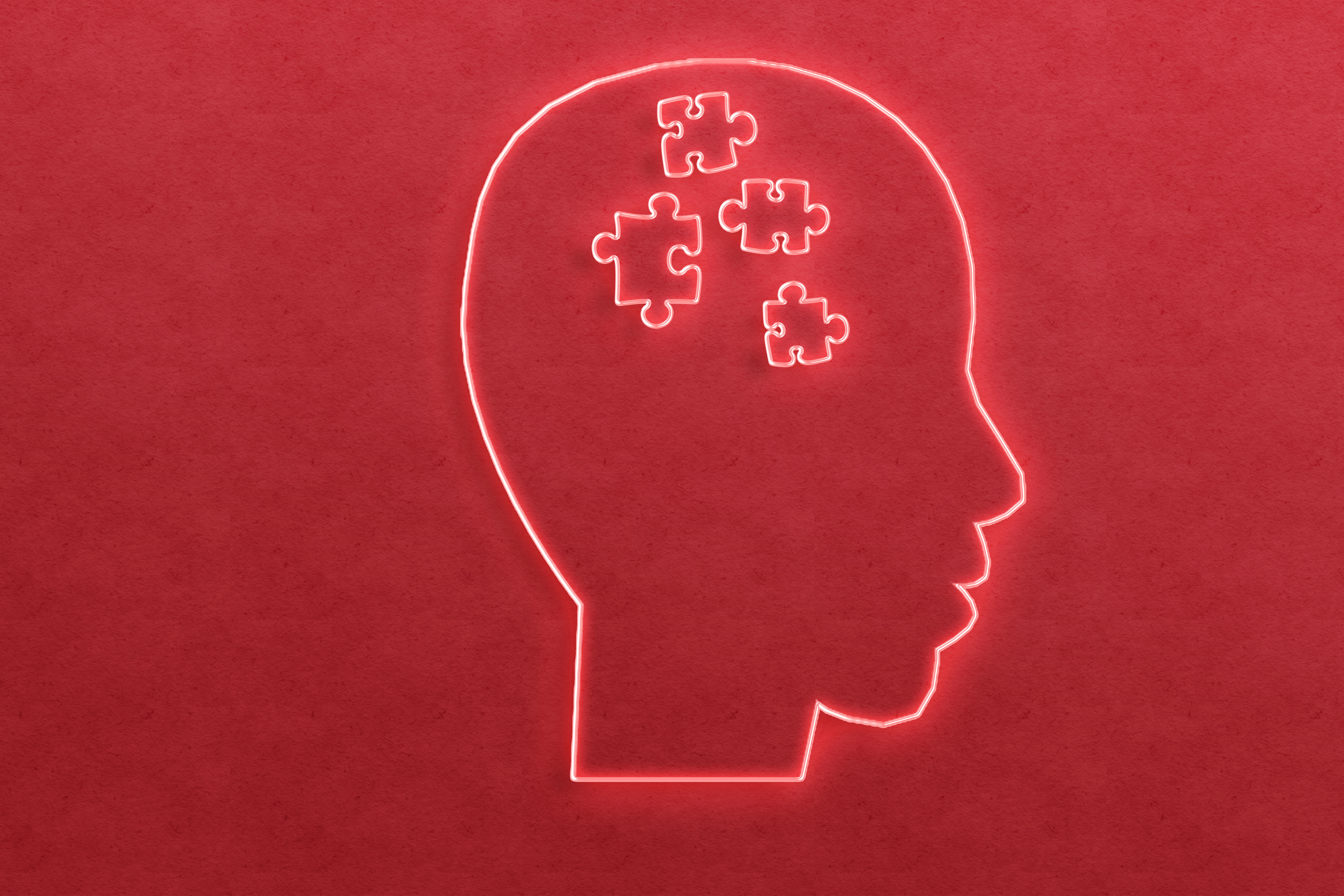 Red wall with a neon light outline of a person's head. Inside the head is puzzle pieces. 