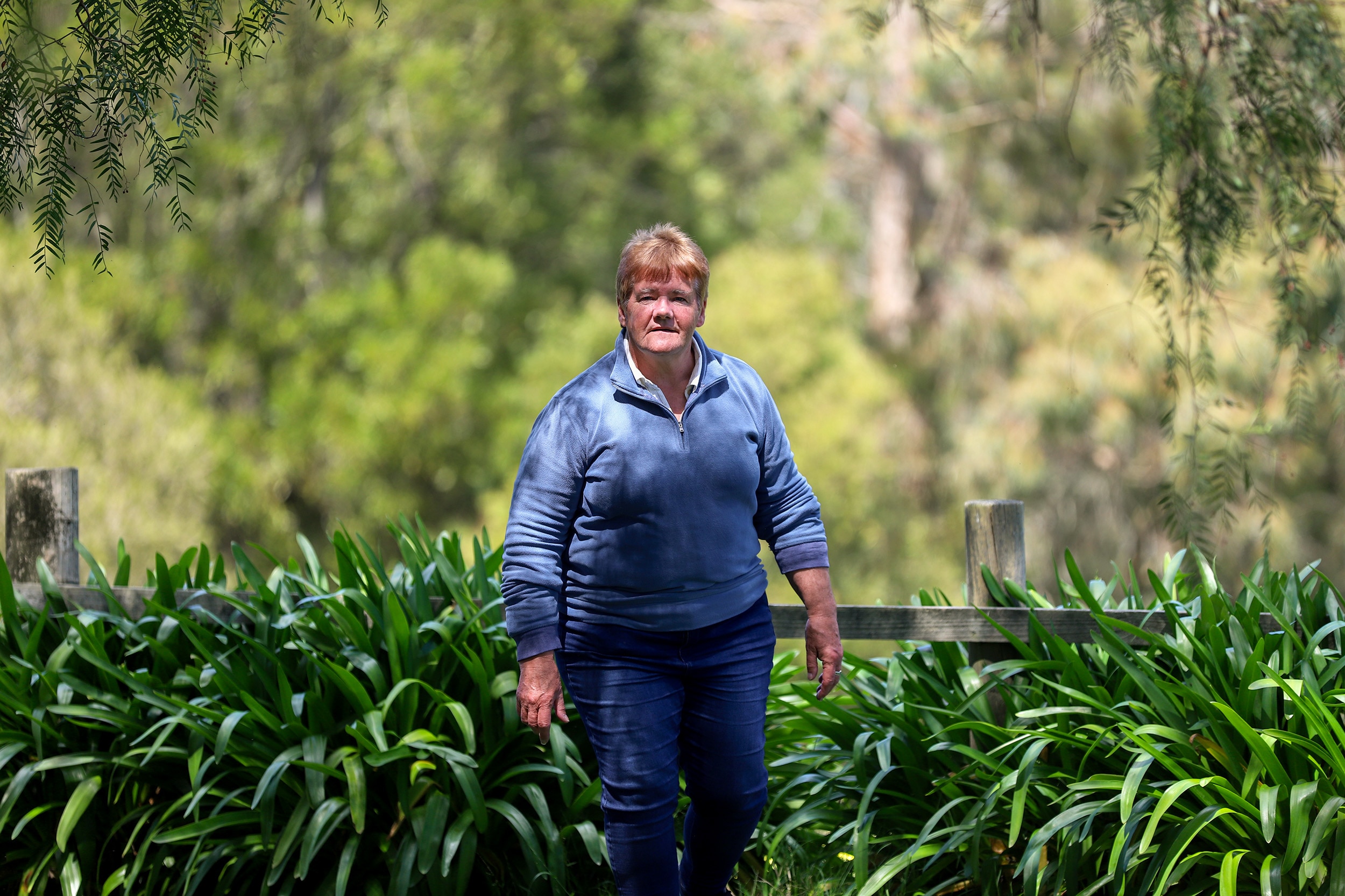Woman wearing blue jeans and jumper stands in leafy green garden 
