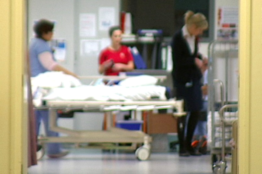Three healthcare workers working inside a hospital room, standing over a bed.
