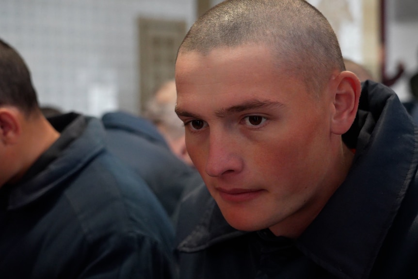 A young man with a shaved head eats in a mess hall.