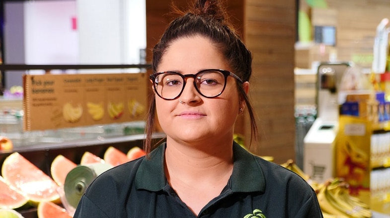 Alyce Veli is dressed in a green Woolworths shirt standing in front of a fruit display inside the supermarket.