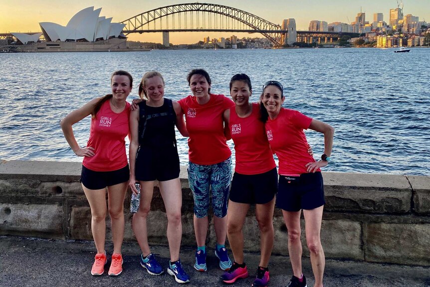 A group of five women pose for a photo with the Sydney Harbour Bridge and Opera House in the background.