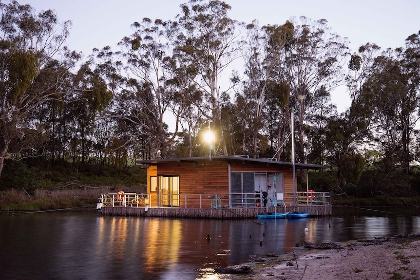 Houseboat-like pontoon building floating on lake among bushland.
