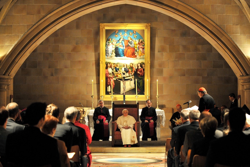 A pope sits in a chair between two cardinals in a glowing church crypt