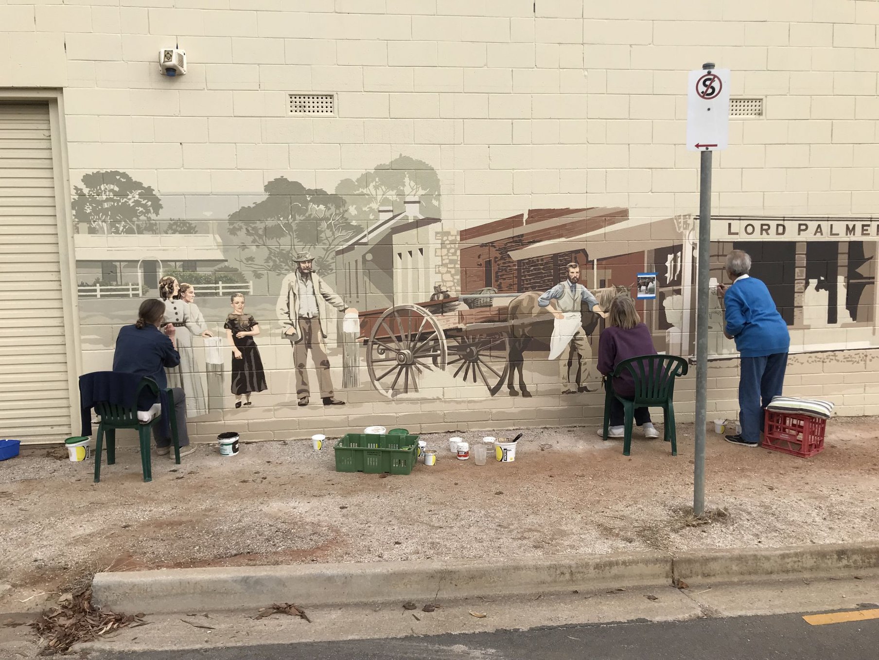 Three people painting a mural on a wall.