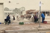 Three people painting a mural on a wall, depicts a historical scene, horse and cart, people dressed in victorian clothing.