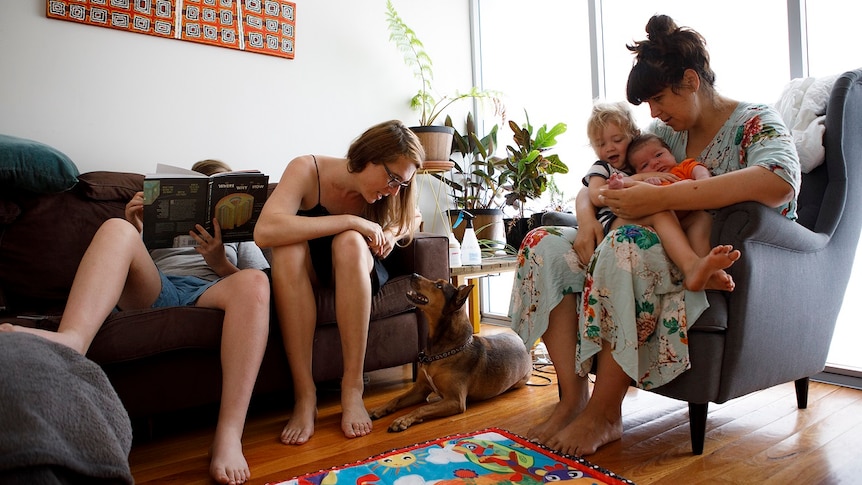 A family of two women and three children sit on lounges in their home with their dog on the floor for story on share housing