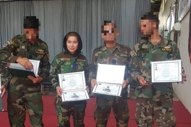 A woman standing with three men all wearing camouflage holding certificates
