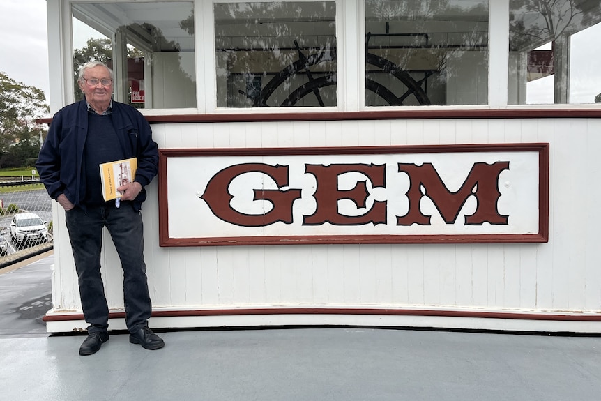 A man standing on a paddle steamer next to a sign that says Gem.