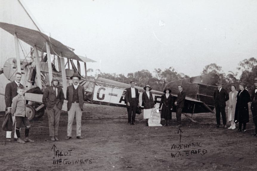 A historic photo of a group of people near an old aeroplane.
