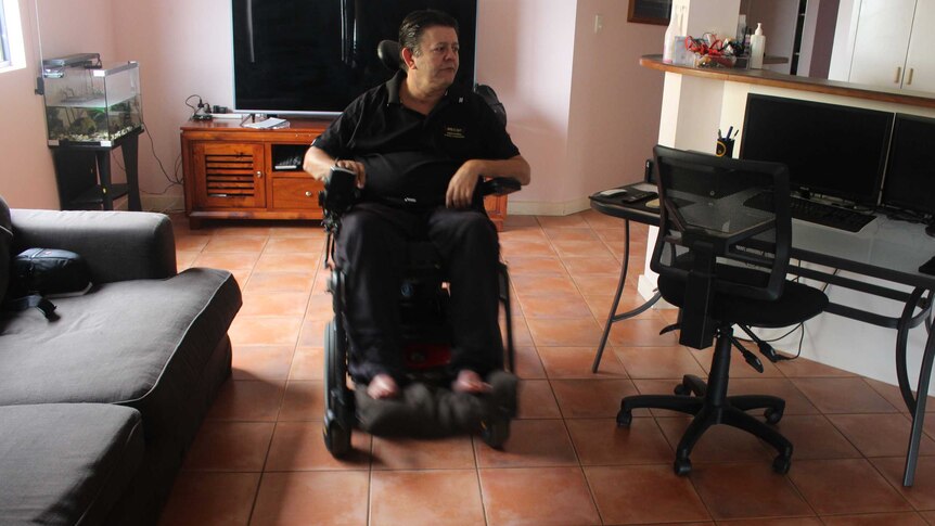 Mark Moodie moves through his living room in a wheelchair