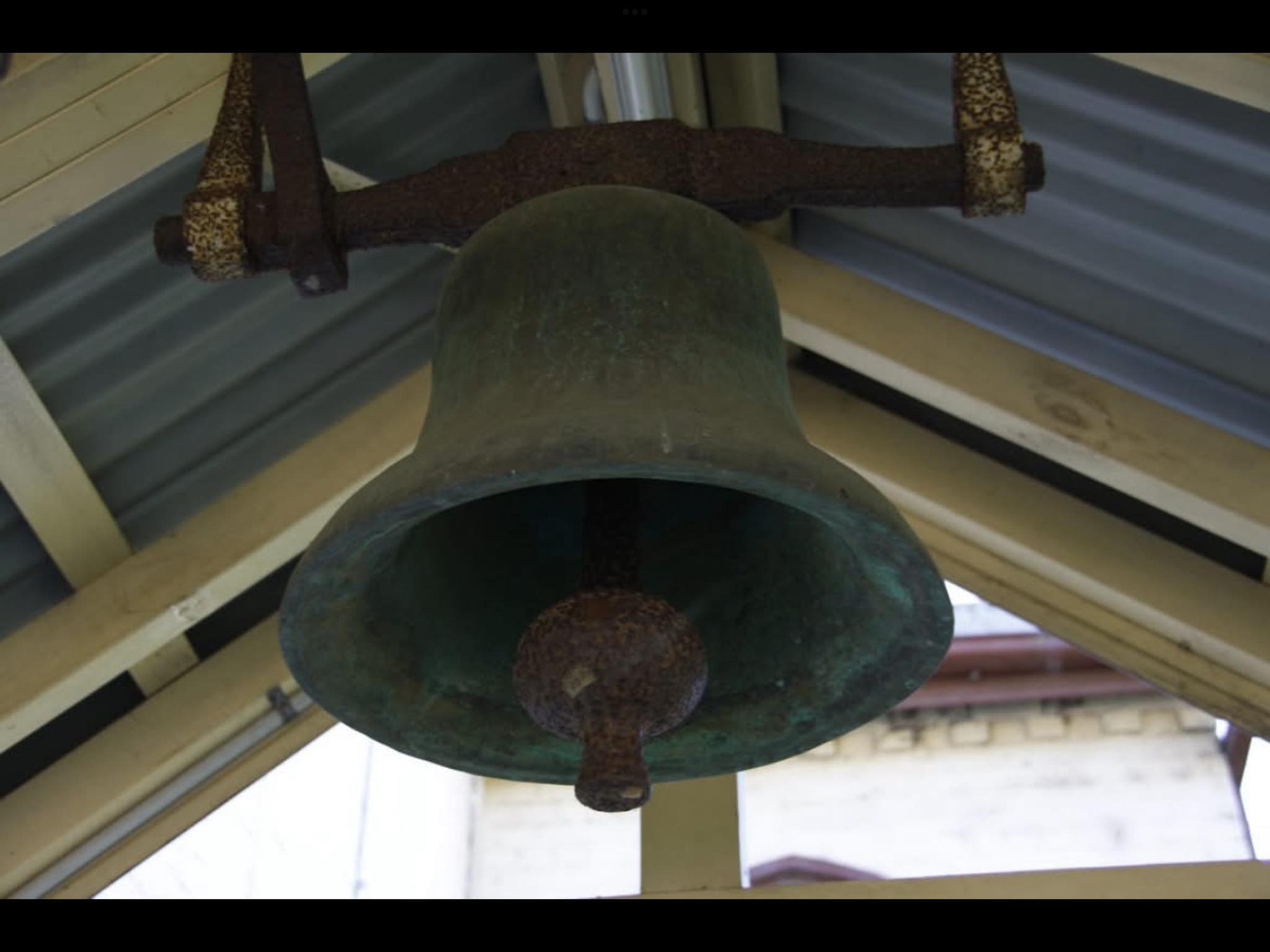 The original church bell, made of bronze, hanging from a roof. 
