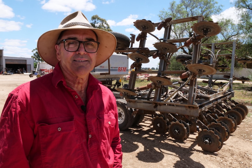 A man standing in front of a rice seeding machine. 