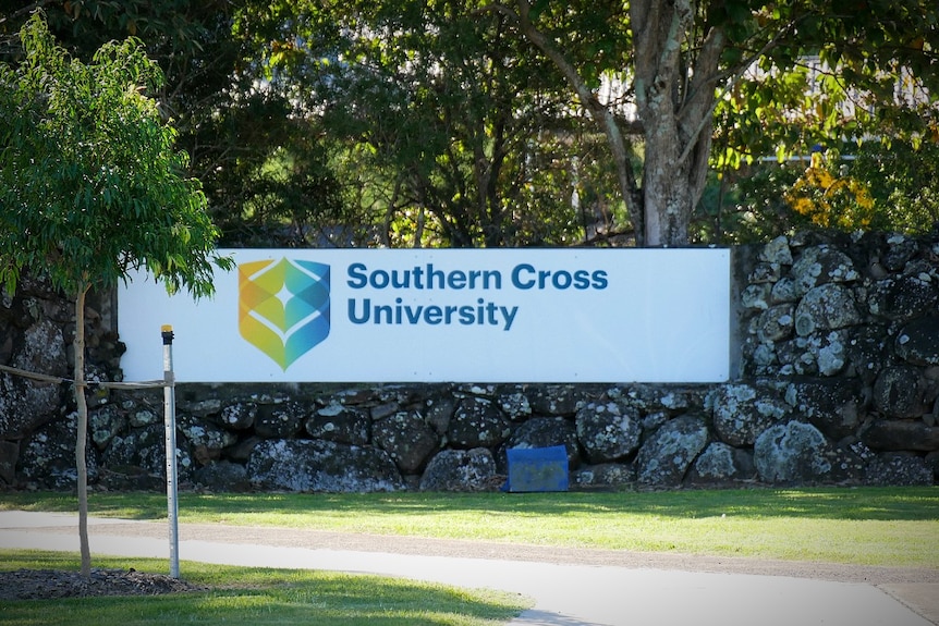 A white sign with 'Southern Cross University' surrounded by trees, grass and a path
