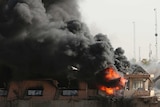 Thick black smoke rises from a damaged warehouse.