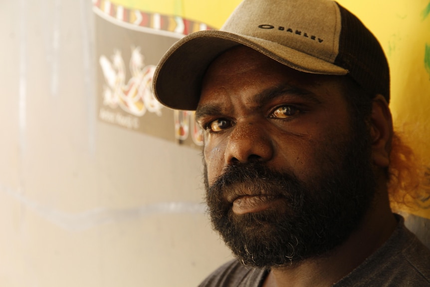 An Aboriginal man with a beard, wearing a baseball cap looks at the camera.