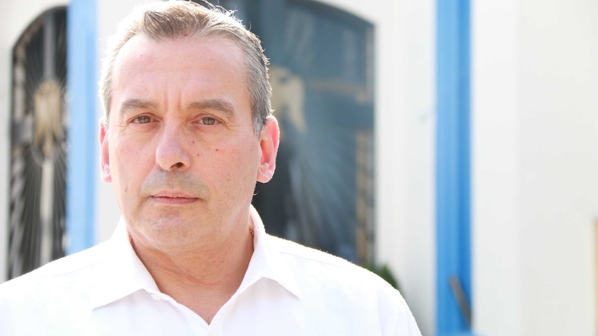 Portrait of middle aged man in white collared shirt in front of a blue, white and gold window frame