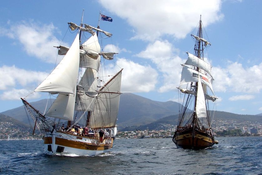 Two tall ships with full white sails on a river