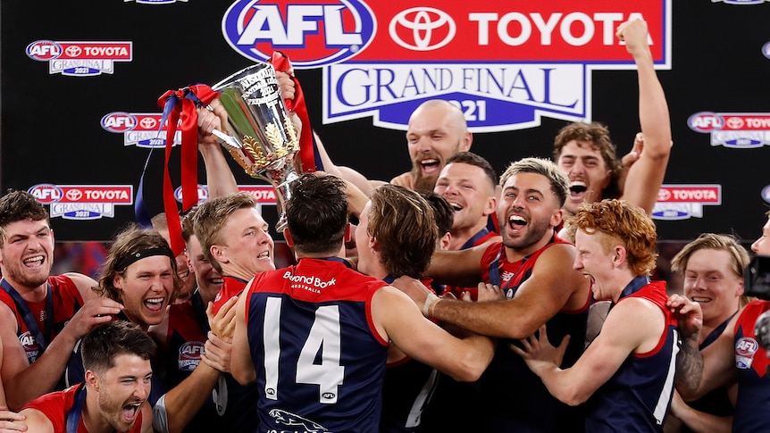Melbourne Demons players smile as they lift the AFL premiership cup on stage at the grand final.