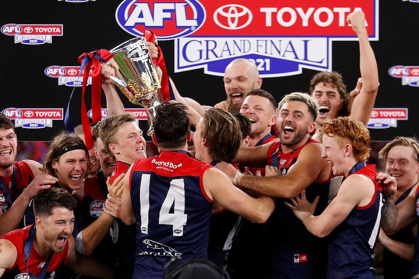 Melbourne Demons players smile as they lift the AFL premiership cup on stage at the grand final.