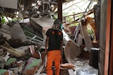 A person with their back to the camera stands amid the rubble of a house.