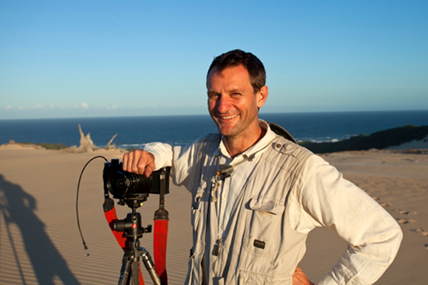 A man on a beach sand dune with a camera.