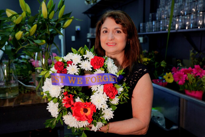 A woman standing in a florist shop holding an Anzac Day flower wreath.