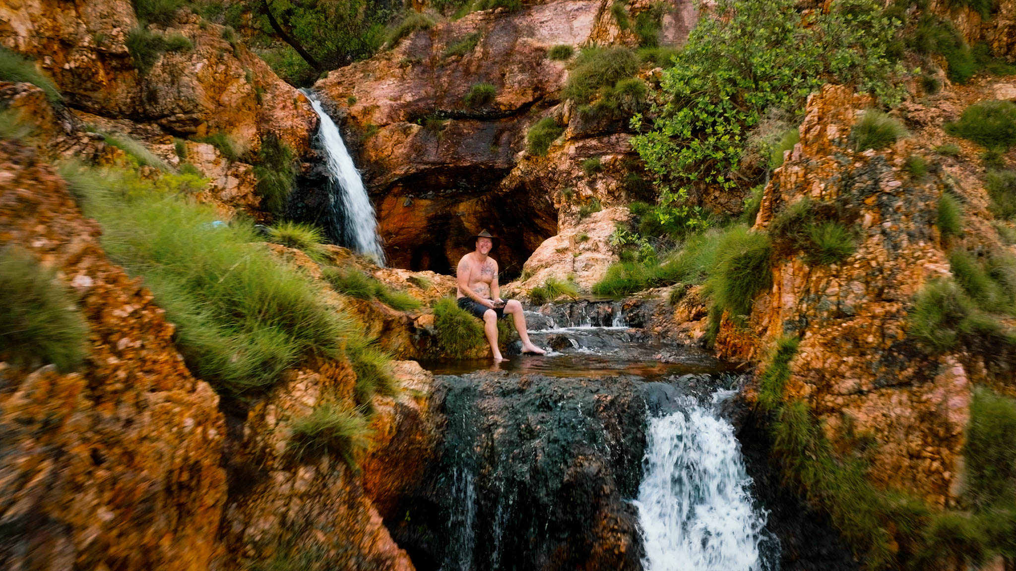 A man sits in a pool among a few small waterfalls