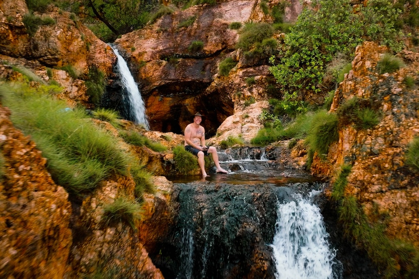 A man sits in a pool among a few small waterfalls