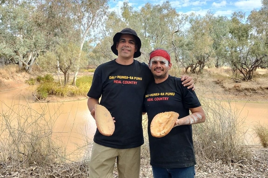 Two men standing by a river holding coolamons