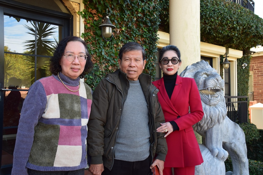 Two Asian women and an Asian man in the centre standing outside a house.
