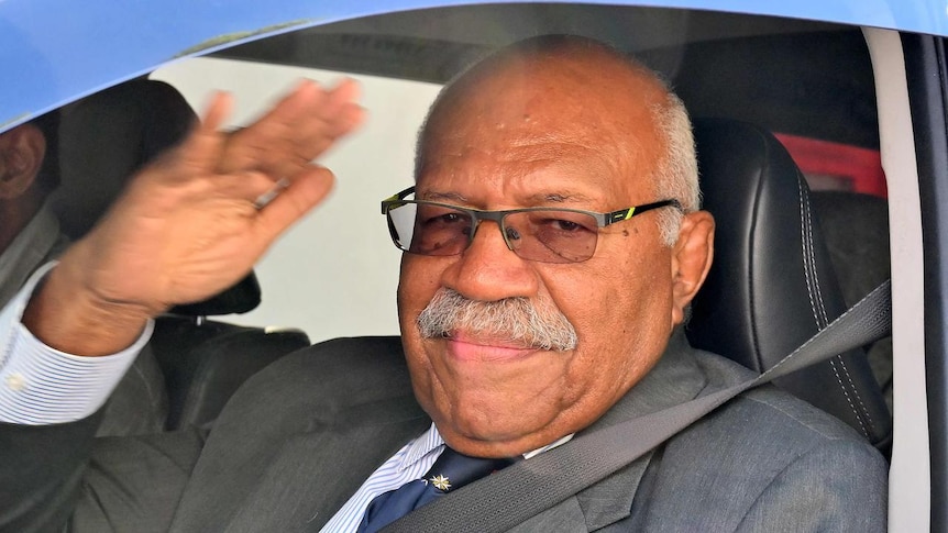 Tight shot of a man, Sitiveni Rabuka, waving from a car.