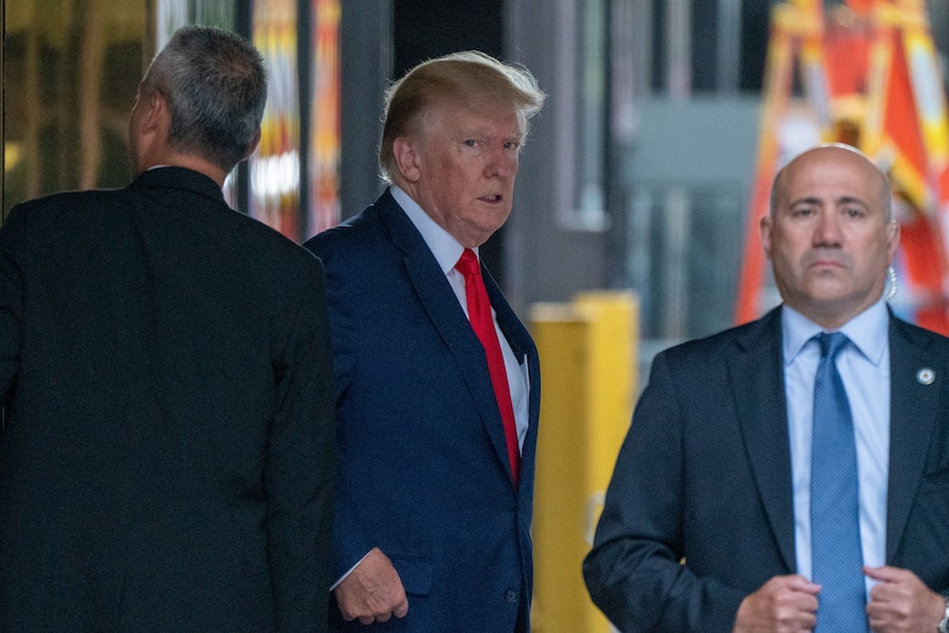 Donald Trump glances at the camera as he exits Trump Tower, flanked by security personnel.