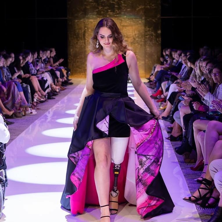 A model with a prosthetic leg walks down a catwalk.