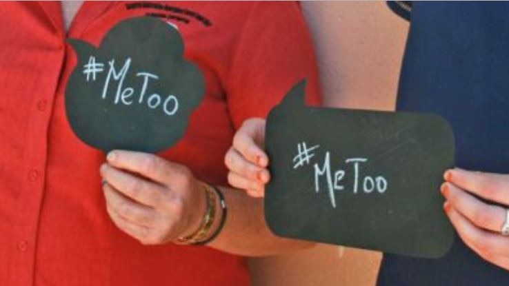 Two women, faces not visible, hold blackboard cartoon caption signs with "#MeToo" written on them