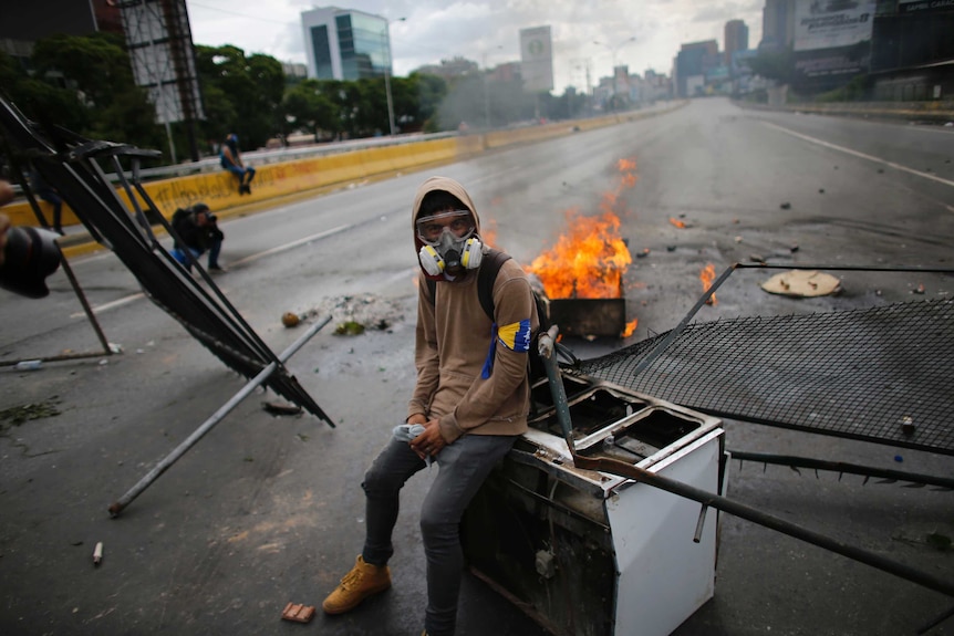 A demonstrator sits on a discarded stove at a barricade.