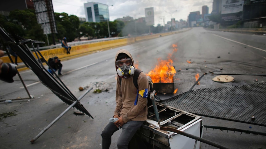 A demonstrator sits on a discarded stove at a barricade.