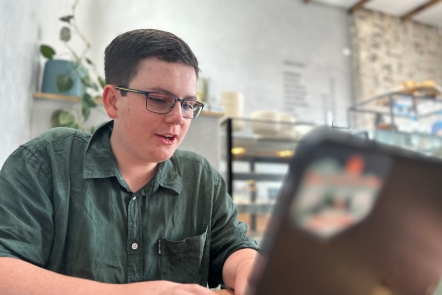 Teenage boy works on laptop from a table in a cafe