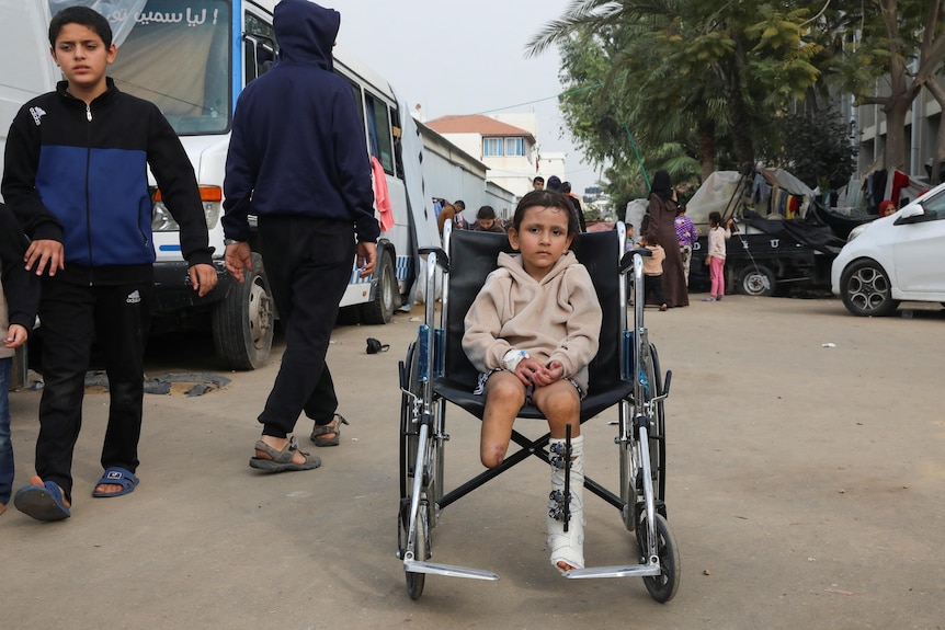A young girl in a wheelchair on a street in Gaza with one leg amputated below the knee and the other in a caste