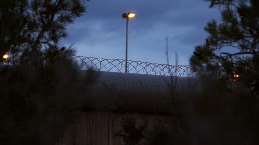A roll of barbed wire atop a prison wall at night.