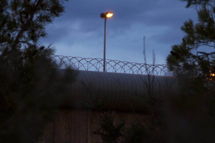 A roll of barbed wire atop a prison wall at night.