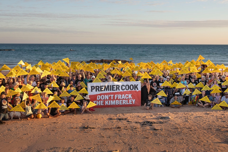 Dozens of people standing on a beach holding signs asking the government to ban fracking.