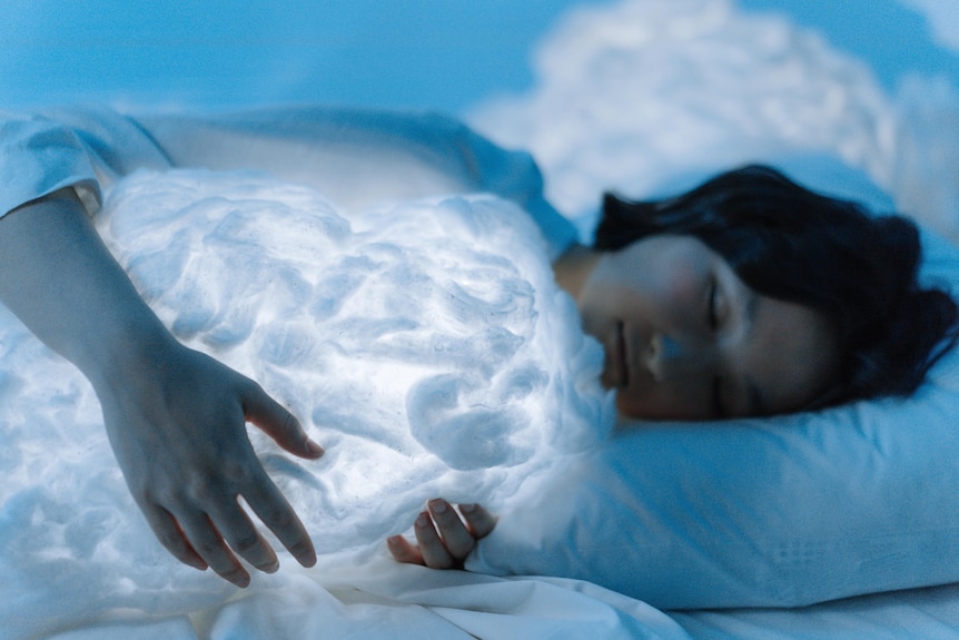 A woman sleeping while holding a glowing white cloud.